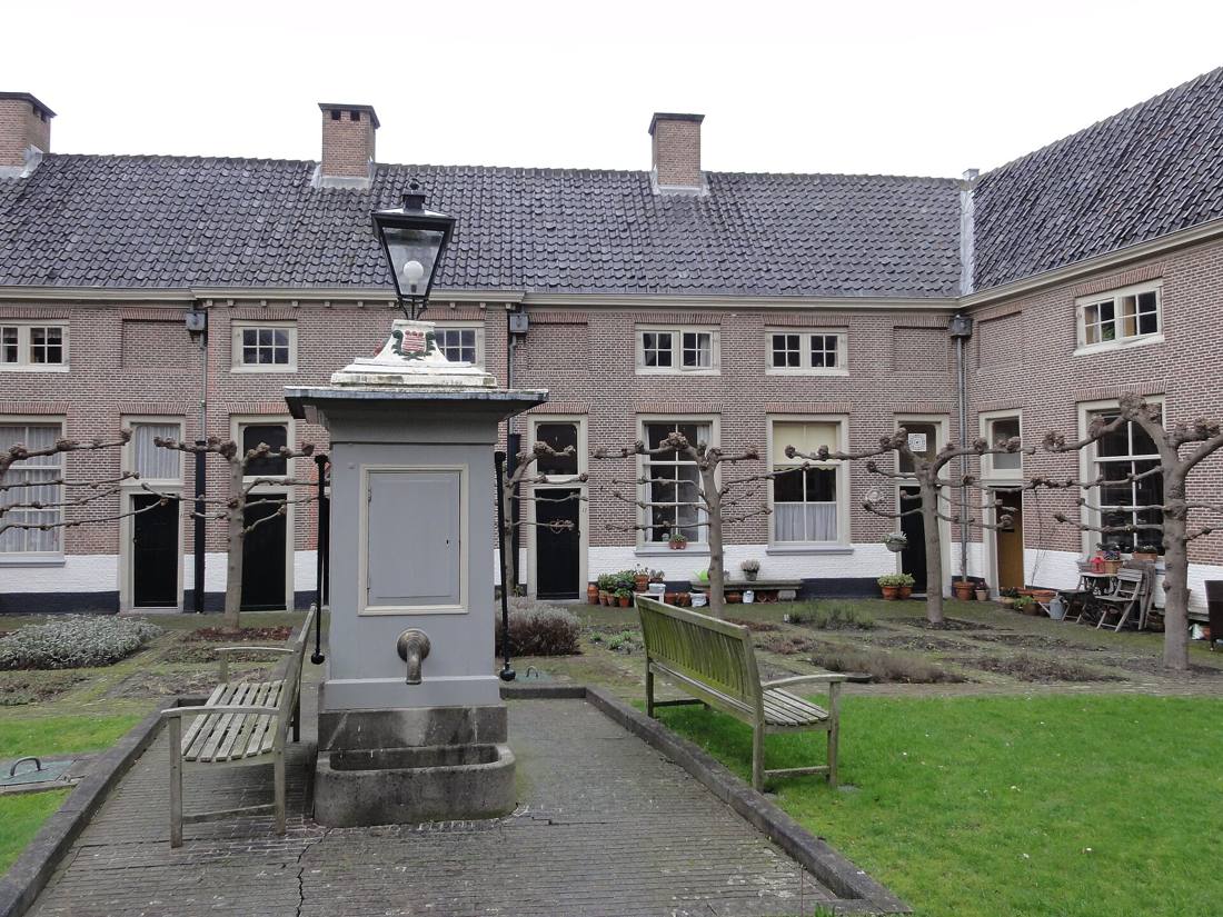 Binnenplaats van het hof met de pomp en lantaarn, leilinden en kruidenperken voor de bakstenen huisjes